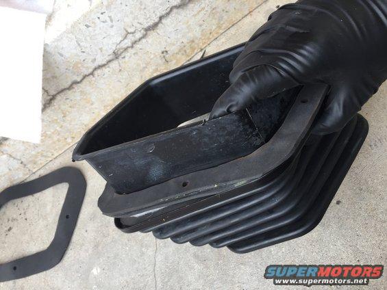 Gloved hand holding a black rubber seal and a black plastic housing with ribbed bellows