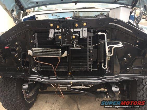 Front of vehicle showing radiator, AC condenser, and engine components. Tires visible
