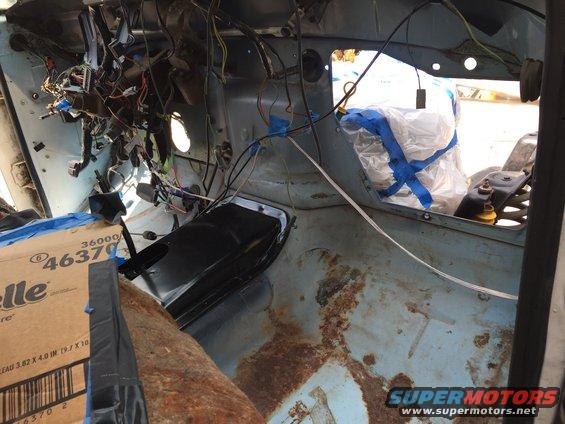 1978 Ford Bronco interior showing exposed wiring and rusted floor panels. A box of paper towels is on the passenger side