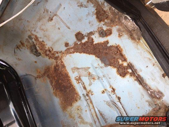 Close-up of a vehicle's floor pan showing significant rust damage and some light blue paint