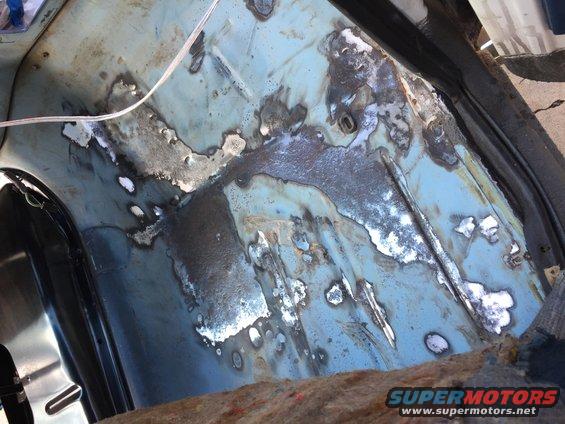 Blue metal floor pan with extensive rust and weld repairs, showing a white wire