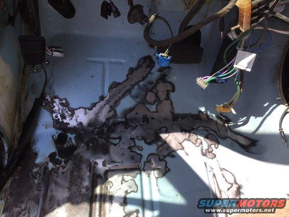 Close-up of a rusted floor pan with exposed wiring harness and connectors