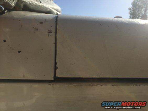 Close-up of a gap between two beige vehicle body panels. Some rust spots visible on the left panel
