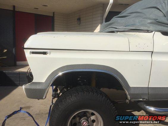 White SUV fender and tire with chrome trim and gray fender flare. A blue strap is visible on the ground