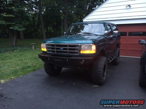 Green Ford Bronco with aftermarket bumper and large tires parked in driveway