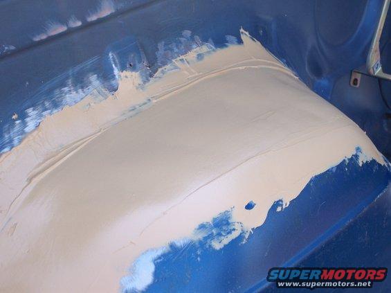 Body panel being filled with putty, showing blue paint underneath