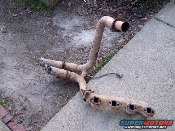Rusty exhaust manifold with four exhaust ports and two pipes leading to a single outlet