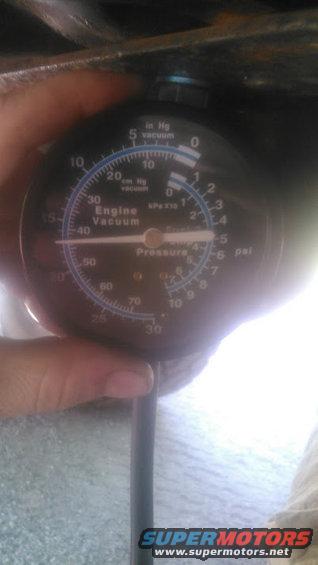 Engine vacuum gauge held by a hand, showing pressure and vacuum readings