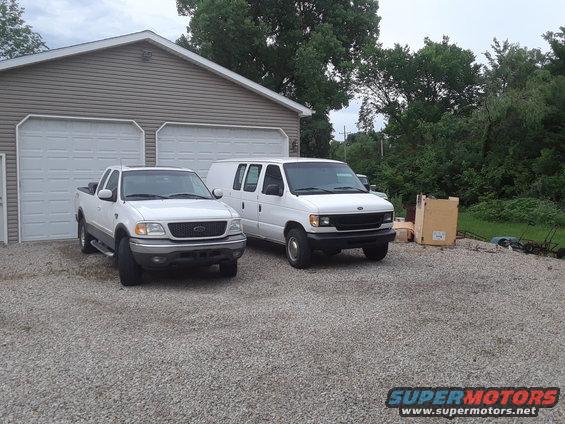 White Ford E-Series van parked next to a white Ford F-150 pickup truck in front of a garage