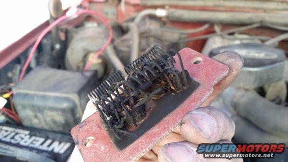 Burned blower motor resistor held in hand, engine bay visible in background