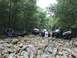 1989 Ford Bronco - Multiple off-road vehicles traverse a challenging rocky terrain in a forest setting.