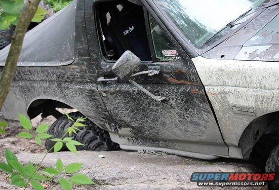Mud-covered 1990s Ford Bronco stuck off-road, showing side door, mirror, and fender badge