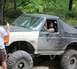 1989 Ford Bronco - A heavily modified Ford Bronco navigates an off-road trail with a driver and passenger visible.