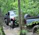 1989 Ford Bronco - Two off-road trucks are shown driving through a wooded area with muddy terrain.