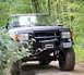 1989 Ford Bronco - A black Ford Bronco navigates a wooded trail, its off-road modifications evident.