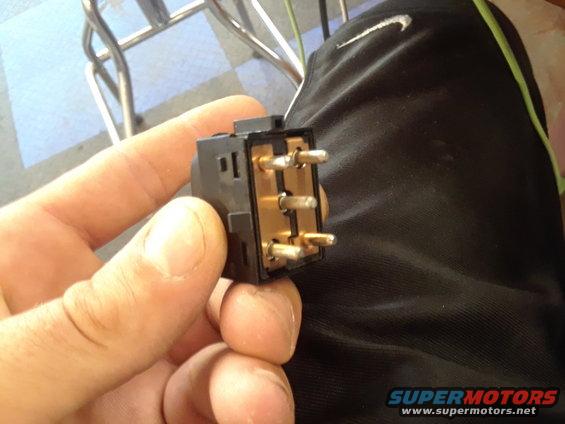 Hand holding a black electrical switch with gold-colored pins