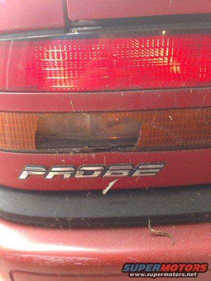 Red car rear taillight assembly with 'PROBE' badge, showing damage to the amber section