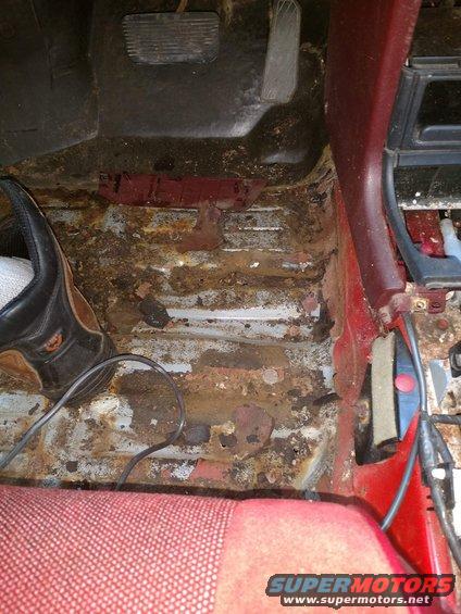 car interior showing heavily rusted floor pan and seat fabric