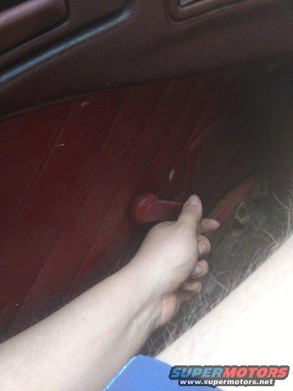 Hand operating a red window crank on a dark red car door panel