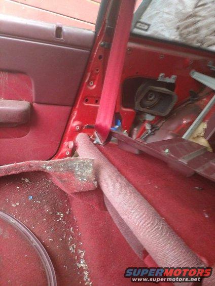 red car interior with seatbelt and door panel removed, showing exposed metal and wiring