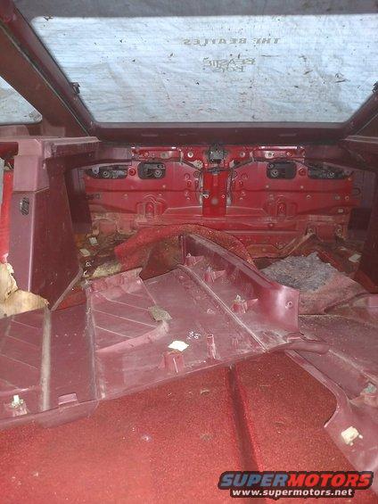Interior rear of a red car with glass roof, showing disassembled panels and carpet
