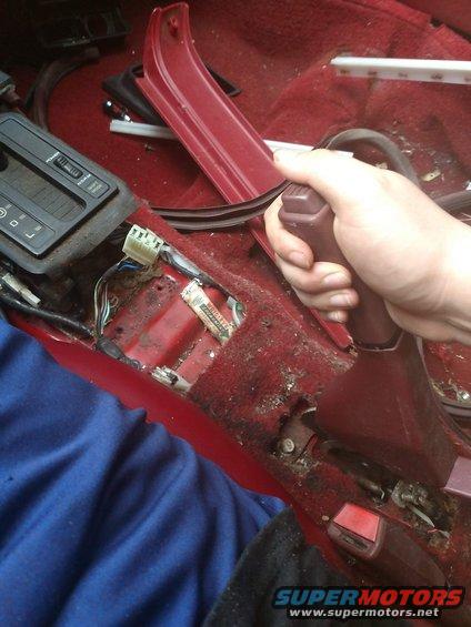 Hand on gear shifter in disassembled car interior, showing exposed wiring and console parts