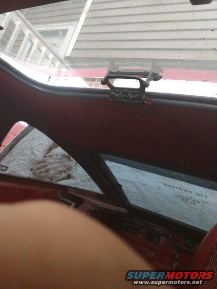 Car interior with red upholstery, a grab handle on the ceiling, and a tarp on the rear window