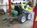 1984 Honda ATC 250 R - A trailer with a green tank and yellow arms is parked in a garage, with a jack supporting the hitch.