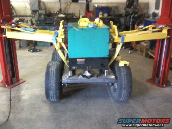 Generator unit on a trailer with four wheels, secured with yellow straps, in a workshop