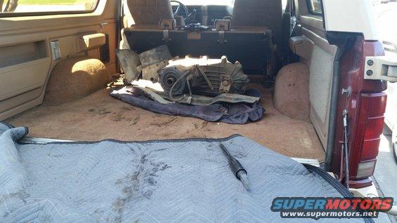 Interior cargo area of a tan SUV with a transmission and parts on the floor