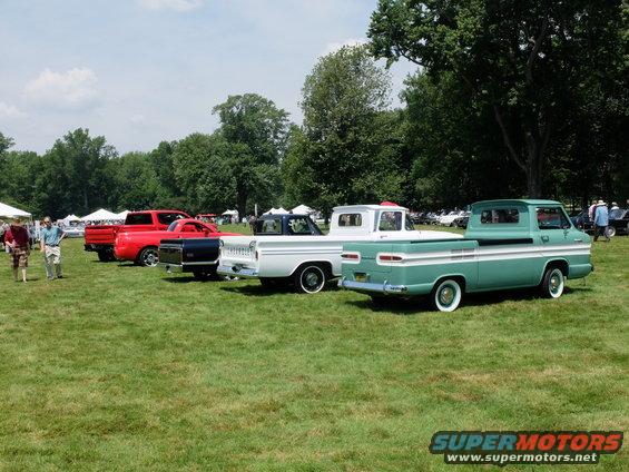 Several vintage pickup trucks parked on grass, including a green one with white trim and a white one with a blue bed