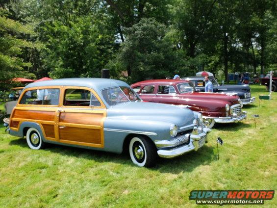 Gray and wood-paneled station wagon parked on grass with other classic cars behind it