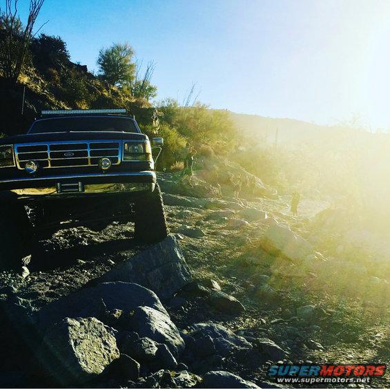Dark blue Ford Bronco on rocky terrain, front 3/4 view, with light bar on roof