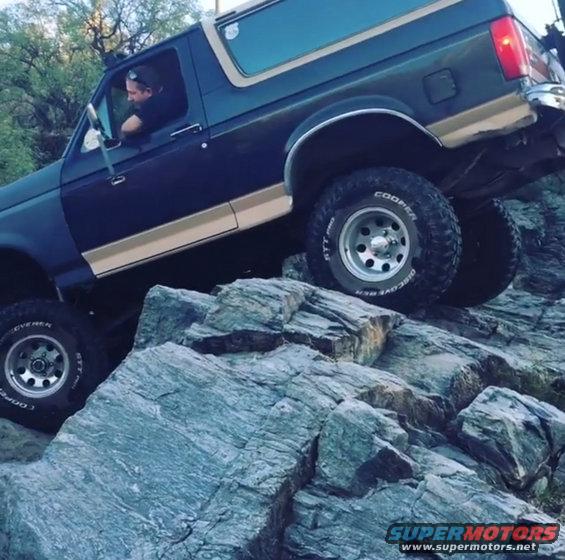 1991 Ford Bronco 3q-front view, dark blue and tan, off-roading on rocks