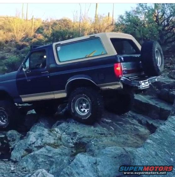 Dark blue 1991 Ford Bronco with tan top driving over rocks in a desert landscape