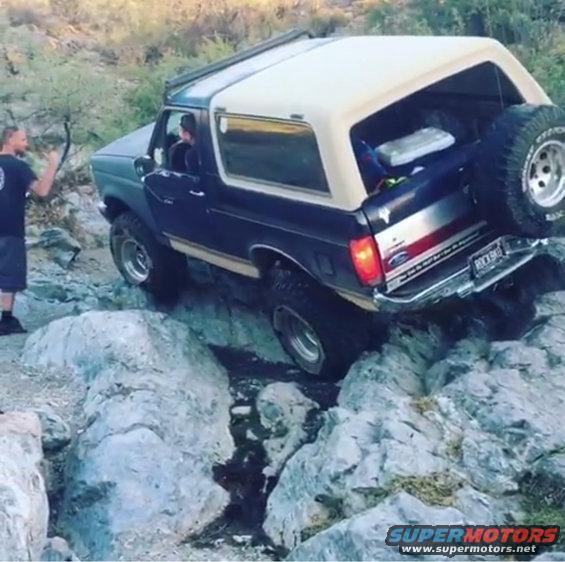 Dark blue and tan Ford Bronco navigating rocky terrain, spare tire mounted on rear