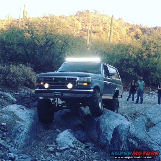 Dark blue 1991 Ford Bronco with a light bar driving over rocks in a desert landscape