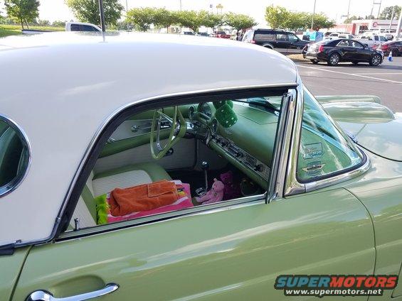 Interior of a light green 1955 Ford Thunderbird with a white roof, showing the dashboard, steering wheel, and seats with towels and a stuffed animal