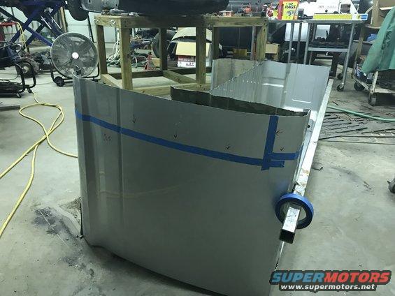 Gray truck bed panel with blue tape markings, seen from a low angle in a workshop