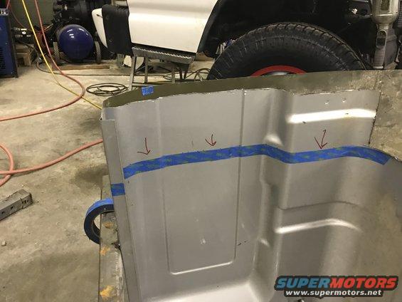 Metal panel with blue tape and red arrows, part of a vehicle repair