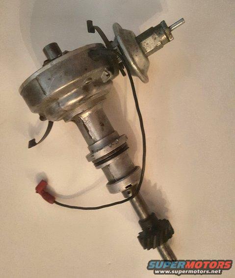 Metal distributor with a black gear and red wire connector against a light background