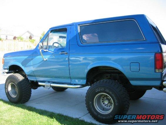 Blue 1989 Ford Bronco with lifted suspension and aftermarket wheels parked on a driveway
