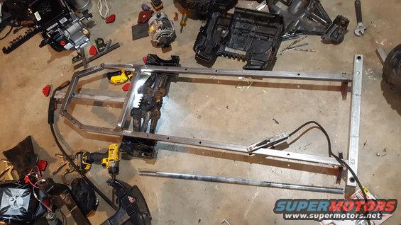 Aluminum frame assembly with engine components, drills, and tools scattered on concrete floor