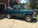 1996 Ford Bronco - Side view of a teal 1996 Ford Bronco with a spare tire mounted in the bed, parked outside a garage.