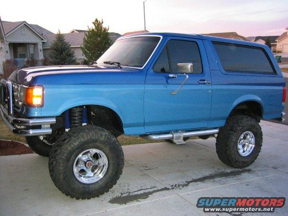 Blue Ford Bronco with large tires and chrome wheels, lifted suspension, and a chrome bumper