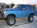 1989 Ford Bronco - This lifted blue Ford Bronco has large off-road tires and chrome wheels, with a chrome bumper and side steps.