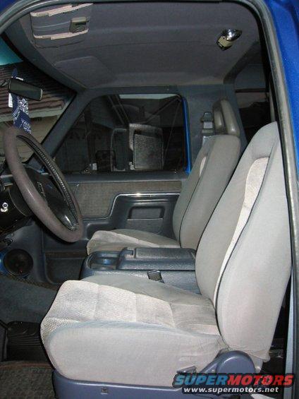 Vehicle interior with gray cloth seats, dark blue dashboard, and steering wheel. A bandana hangs from the rearview mirror
