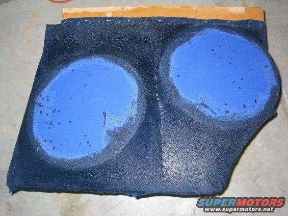 Dark blue fabric-covered subwoofer enclosure with two circular blue speaker cutouts, mounted on wood