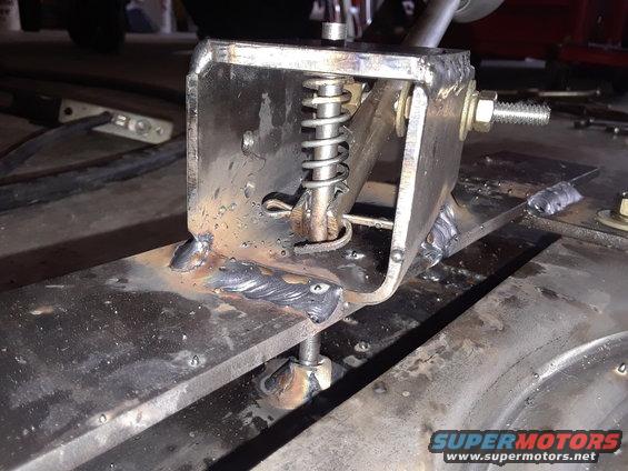 Close-up of a welded metal bracket with a spring mechanism, possibly part of a vehicle's suspension or a custom modification