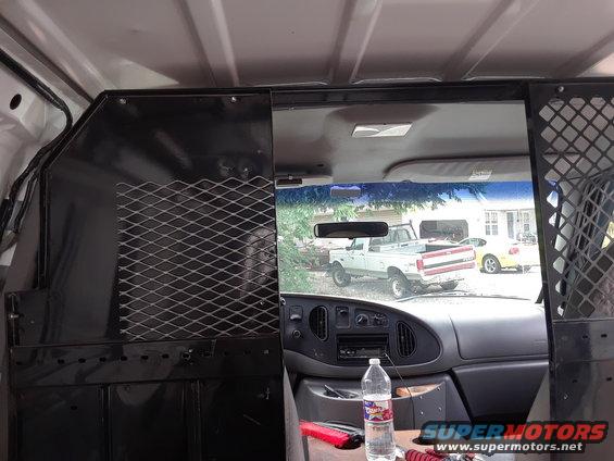 View from inside a van, looking through the windshield at a white pickup truck and a yellow car parked outside